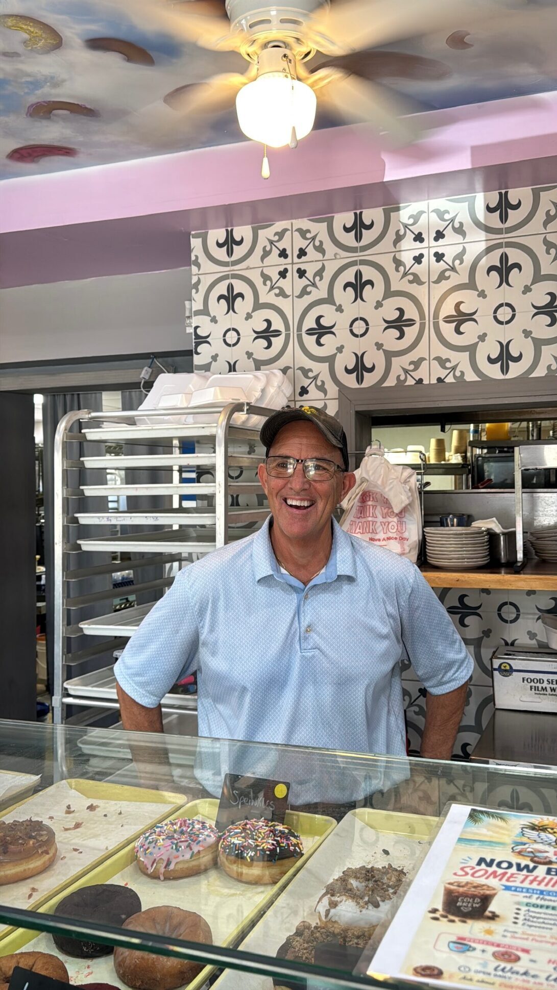 Morgan behind the counter, smiling, with the painted donut ceiling visible above