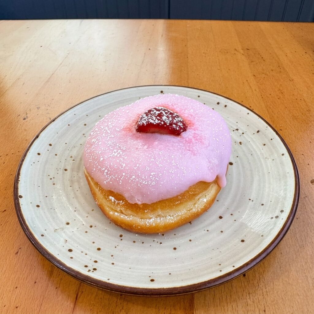 Pink strawberry donut with fresh strawberry and powdered sugar